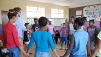 A teacher and a group of students stand in a circle holding hands.