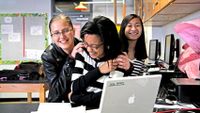 Three girls smiling and laughing around a laptop computer