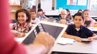 Students use tablets for formative assessment while a teacher in the foreground leads them.