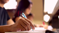 A photo of the arm and hand of a high school male, writing in his notebook.