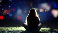 Girl from behind sitting on the ground in spotlight