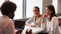 A teacher sits and talks with a student and her mother.