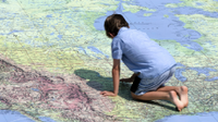 A photo of a young boy kneeling on a giant map of the world.
