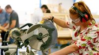 Girl operating a large table saw wearing safety headphones and goggles
