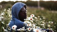 Older boy with grey sweatshirt hood on sitting in a field of daisies