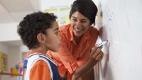 A teacher works at the white board with a young boy.