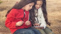 Two young girls sitting outside looking at a tablet device
