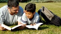 A man and boy reading on the lawn in the backyard