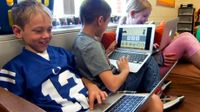 Three kids sitting in class on a big futon each with a laptop