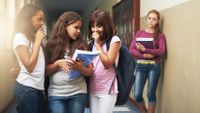 Three girls exclude another girl in a school hallway.