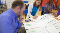 Three educators are sitting at a paper-covered table, reading and taking notes.