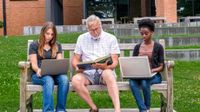 Three adults sitting side-by-side on a bench working on their laptops