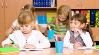 A young girl cheats by looking at another student’s work.
