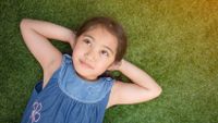 A young girl lies on her back, relaxing on the grass.
