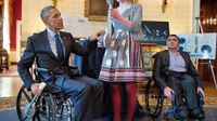President Obama sitting in a wheel chair speaking with a student