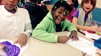 Three elementary school children sitting together at a table in class coloring with markers