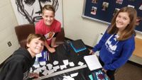 Three students photographed from above work on a project together at a small table