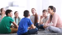 A teacher and her students sit in a circle on the floor.