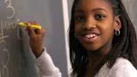 Young African American girl smiling holding chalk in front of a black board