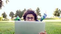 Boy laying on the lawn peeking out over his laptop