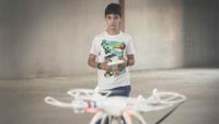 A young boy is standing in an empty cement building. He's playing with a flying, remote-operated drone.