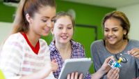 Three teenage female students looks at a computer tablet together.