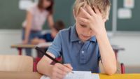 Young boy sits at desk with a confused look on his take while taking a test.