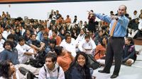 Principal with arms raised talking to a gym full of kids sitting on the floor