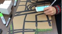 A photo of a student drawing on a piece of cardboard with black marker.