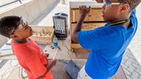 Two boys working with wood and circuits wearing goggles discussing a project