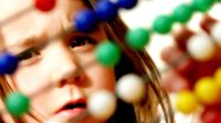 A young girl is intently looking at a wooden Abacus counting number frame, moving the colorful balls along the wire frames.