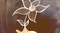 Someone's hand is beneath a chalkboard drawing of a flower, making it look like they're holding the flower in their palm.