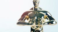 A closeup of an Oscar award, a small, golden statue of a standing naked man. His hands are in front of him, below his chest, holding a wreath.