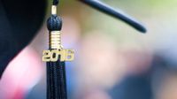 A black graduation tassel with 2016 in gold lettering is hanging from a black graduation cap.