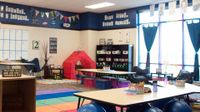 A large, studentless classroom, with large blue bouncy balls, sofa chairs, folding chairs, a tent, crates, mats, and other unique furniture.