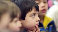 A closeup of the side of a young boy's face. He's looking in front of him. Other young kids are sitting around him, but they are out of focus.