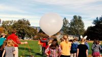 A classroom of kids and teacher out on the field getting ready to release a weather balloon
