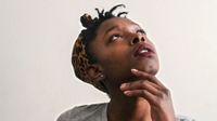 A closeup of a young teenage girl looking up with her head tilt back and her hand under her chin.