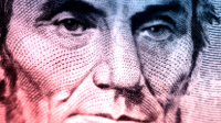 A closeup of president Lincoln's red, blue, and purple face on the five-dollar bill.