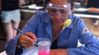 Girl wearing safety goggles heating up a pink liquid on a Bunsen Burner