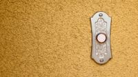 A closeup of a doorbell against a tan, textured wall.
