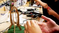 Two kids are using hot glue guns, working at a crafting station, piecing together creative looking buildings to scale.