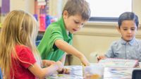 three children working at a desk with hands-on materials