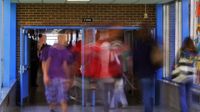 High school students are walking through one school hallway into another through opened double doors. The students are blurred as to imply fast movement and the passing of time.