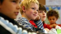 Three young boys are sitting in class, looking towards the front of the room, smiling.