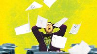 A teenage boy is sitting in a classroom by himself. His hands are on his head, his head is tilted back, his eyes are closed, and he's yelling. A handful of papers are up in the air around him, falling down.