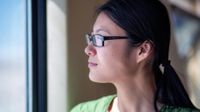 A side shot of a young female teacher in glasses and a green shirt looking out of a window.