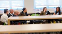 Nine adults are sitting around a table in a library, talking.