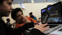 Two students are working together on creating a game project on a computer.