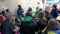 A student is speaking in front of the classroom among his friends listening to him.